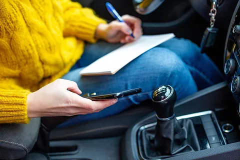 persona en el coche con libreta y teléfono